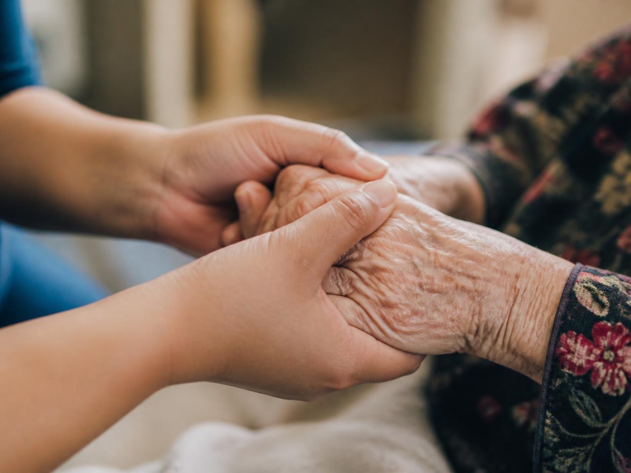 A caregiver gently holding an elderly person's hands